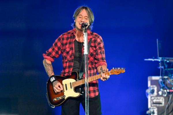 Keith Urban holding a guitar and singing into a microphone at the 2024 iHeartRadio Music Festival in Las Vegas, Nevada